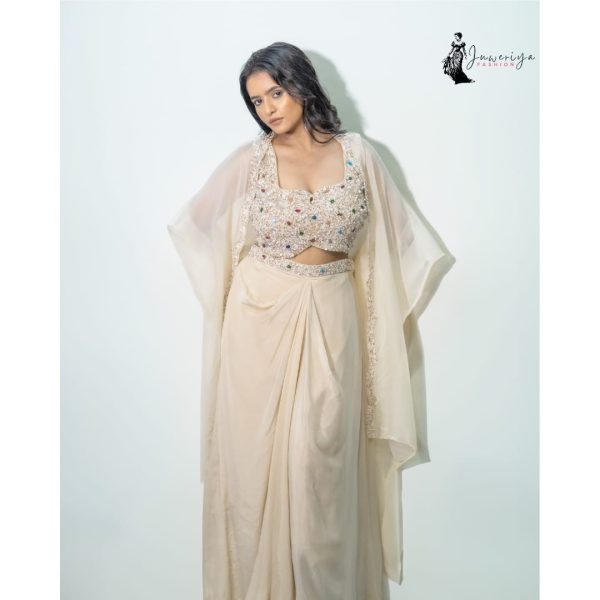 Model wearing an elegant cream-colored embellished crop top with matching draped skirt and sheer cape designed by Juweriya Fashion